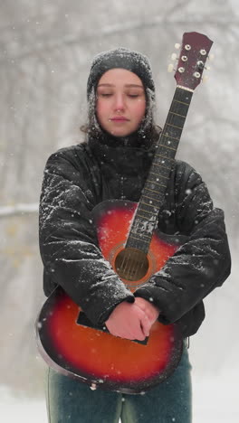 joven de pie en un parque nevado sosteniendo una vibrante guitarra acústica roja, rodeada de árboles helados y nieve que cae suavemente, capturando un momento de invierno pacífico y sereno lleno de música