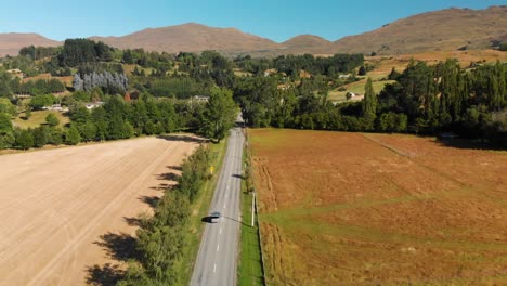 SLOWMO---Luxury-minivan-driving-on-the-road-near-Arrowtown-and-Queenstown,-New-Zealand-with-mountains-in-background