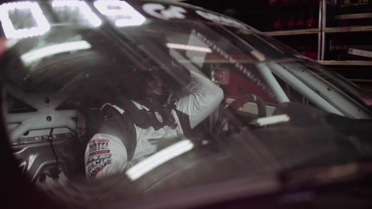 Race car driver inside race car in box garage getting ready for his stint at the ADAC Nurburgring twentyfour hour race on the track. Adjusting his seatbelt.
