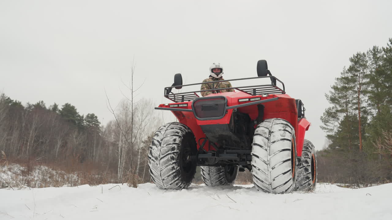 ATV rosso che sfreccia nella neve, pilota con casco che fa un piccolo salto, alta spruzzata di neve, angolazione della telecamera bassa, sfondo di pineta, pneumatici con battistrada robusto che affondano nel sentiero ghiacciato, potente fuoristrada invernale.