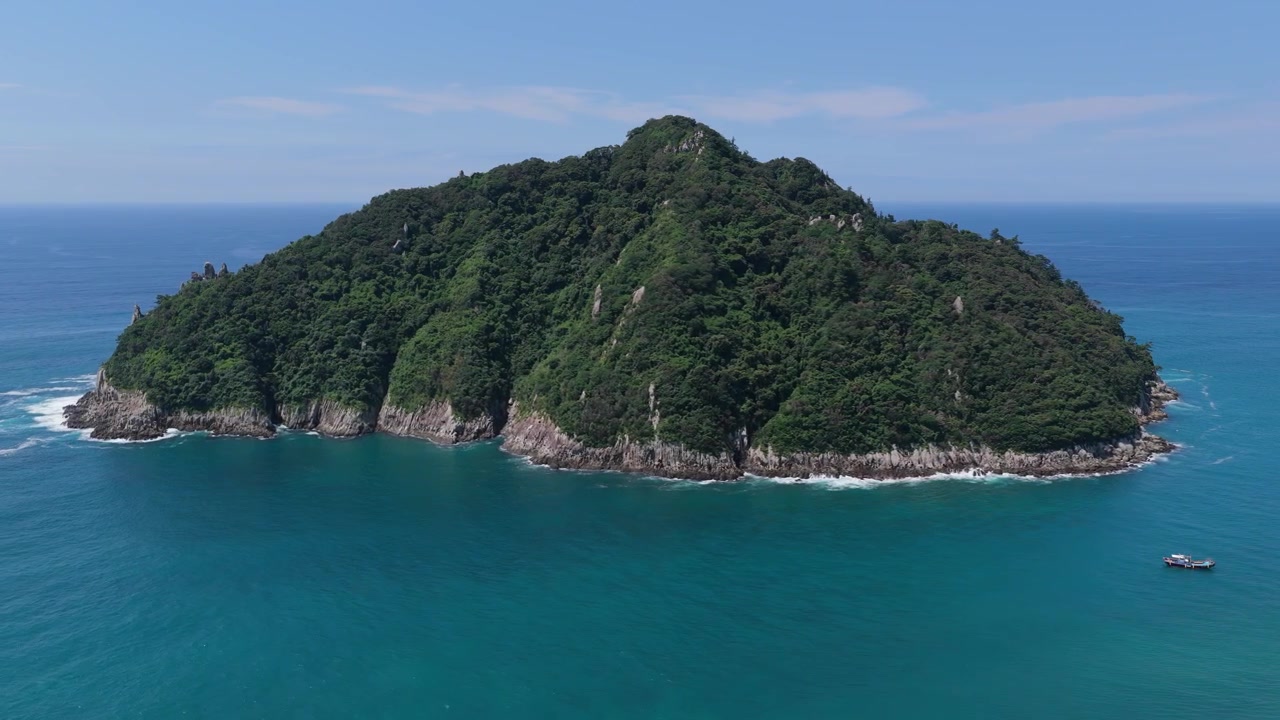 Aerial view of Socheonji Island near Seogwipo, Jeju Island, South Korea, surrounded by clear blue water under a bright sky during a slow leftward pass