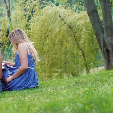 Two-young-women-relax-in-the-park-and-use-a-tablet-1