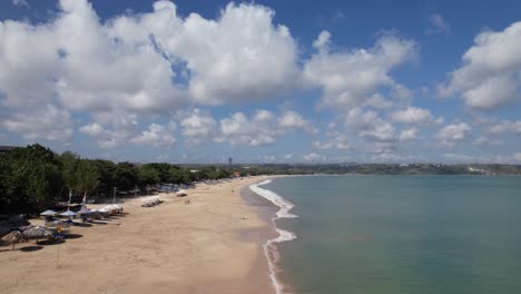 video aéreo sobre la playa de jimbaran en bali, denpasar, indonesia durante un día soleado con olas calmantes