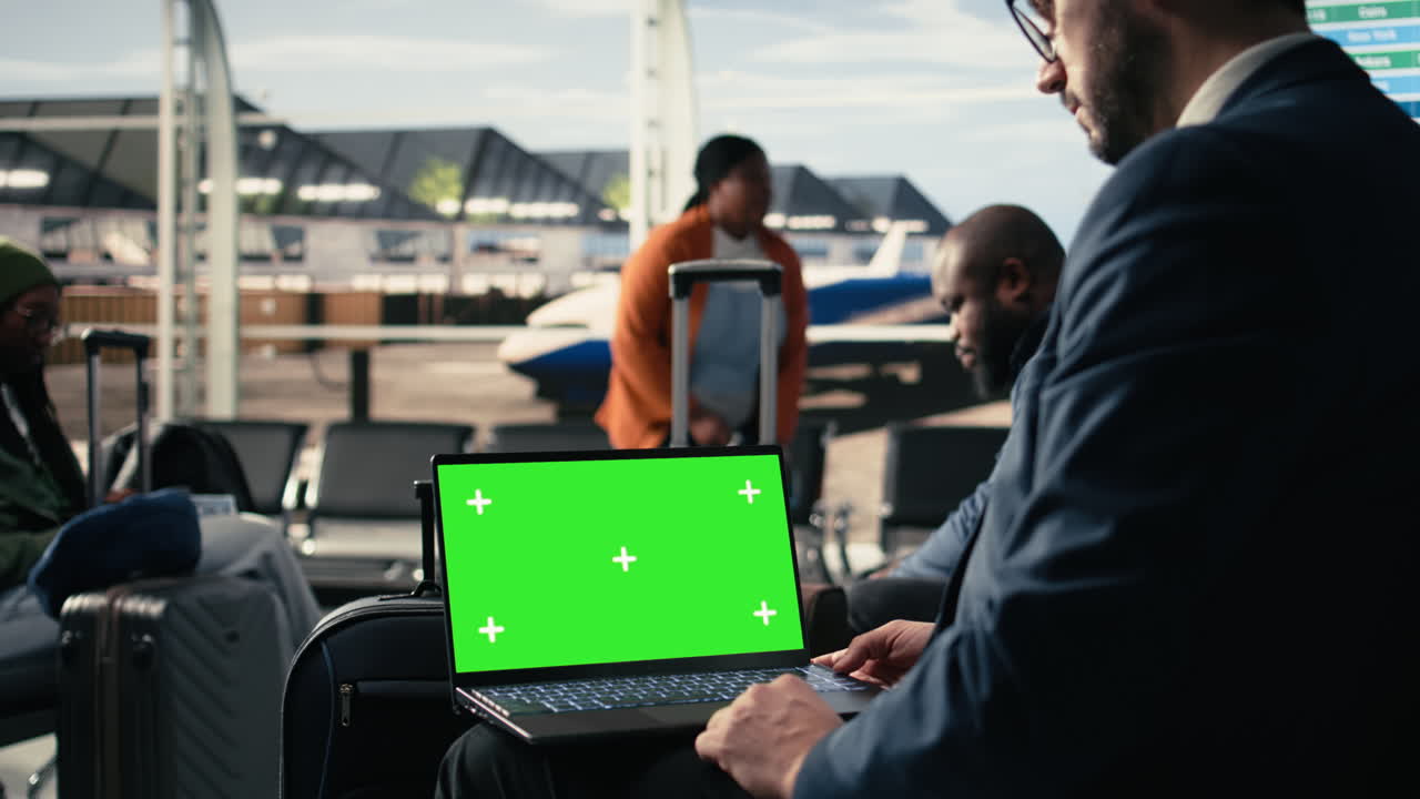 Laptop con schermo verde, terminal aeroportuale affollato, folla di passeggeri diversi.