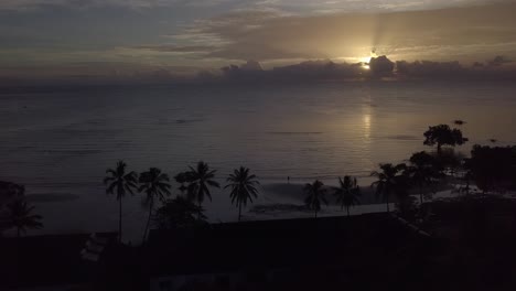 palawan,golden sunrise,sun behind clouds,silhouettes of palm trees and reflection of sun on calm water,aerial wide shot,backwards slowly.