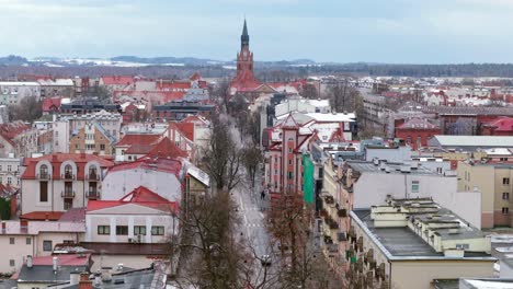 snow over elk cityscape with church of the sacred heart of jesus in view, colorful buildings and neighborhood in winter, armii krajowej street, establishing drone shot