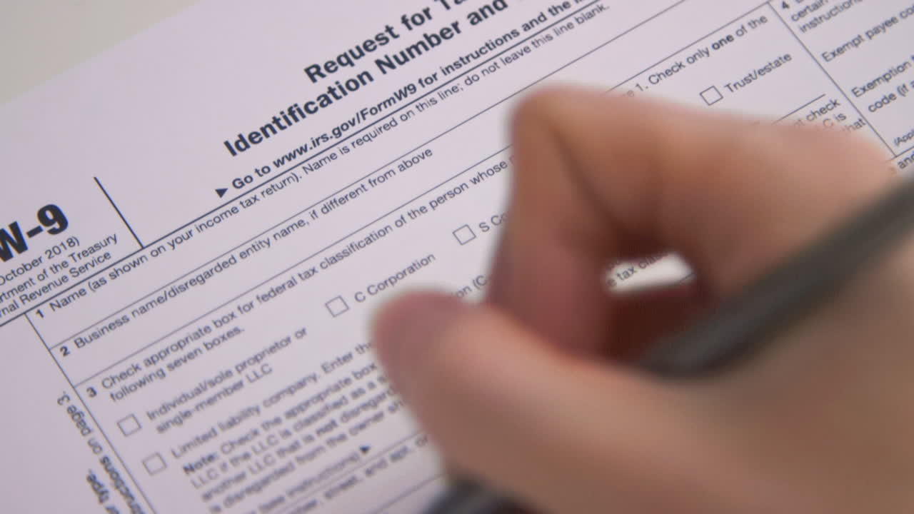 A caucasian woman's hand fills out Tax Form W9 for the IRS