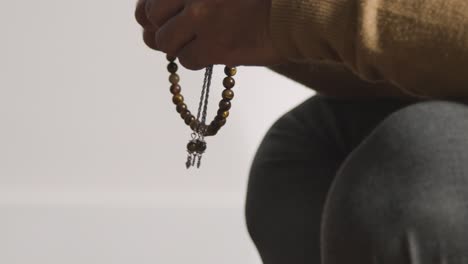 Close-Up-Of-Muslim-Man-Praying-Holding-Prayer-Beads-Against-White-Background