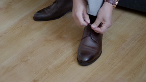 primer plano de zapatos de cuero brillantes siendo atados por el novio durante los preparativos de la boda
