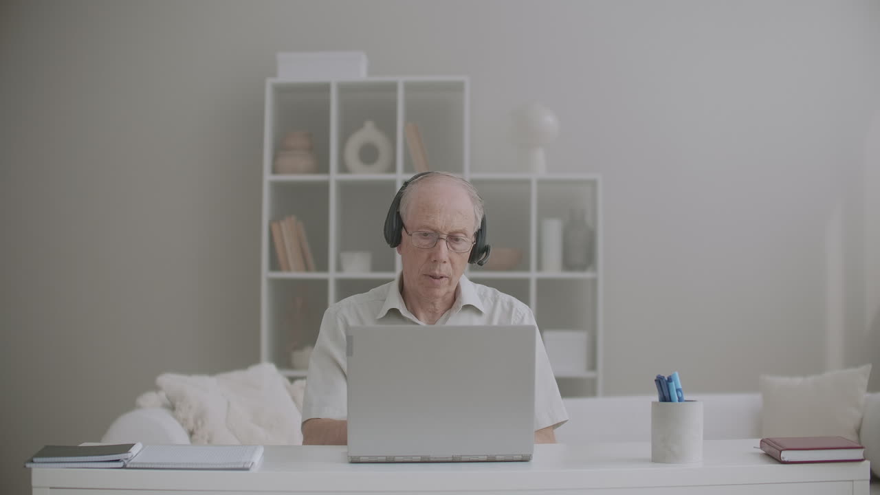 aged male teacher is giving lectures online staying home using laptop with internet connection and headphones