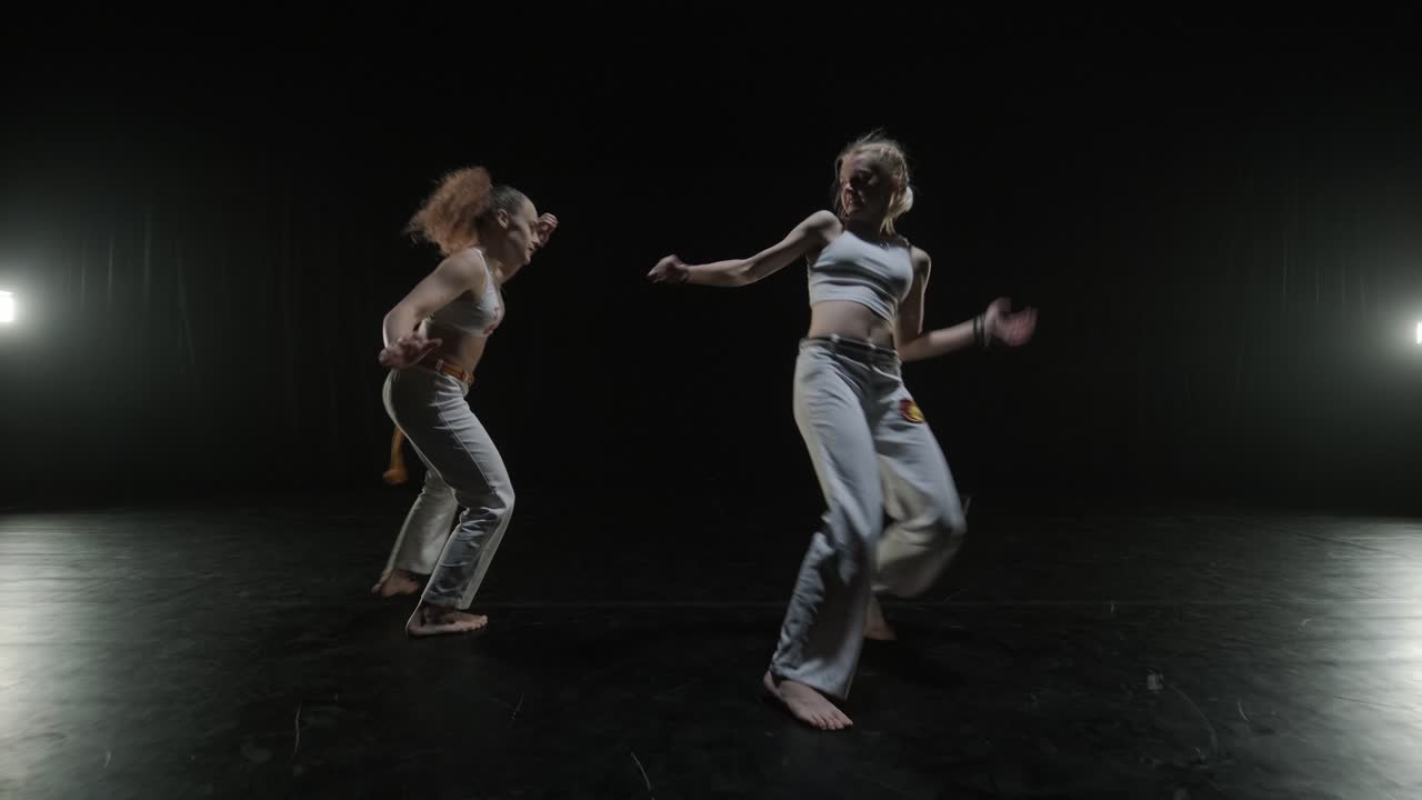 un grupo de bailarines profesionales están practicando capoeira en la oscuridad contra un foco de luz en un fondo negro de estudio. arte marcial afro-brasileño que combina elementos de la danza.