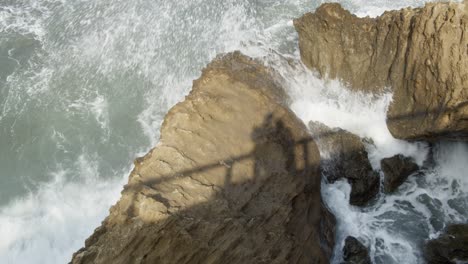 Slow-Motion-Wild,-Strong-Winter-Waves-Crashing-on-Rocks-with-Shadow-of-a-Couple