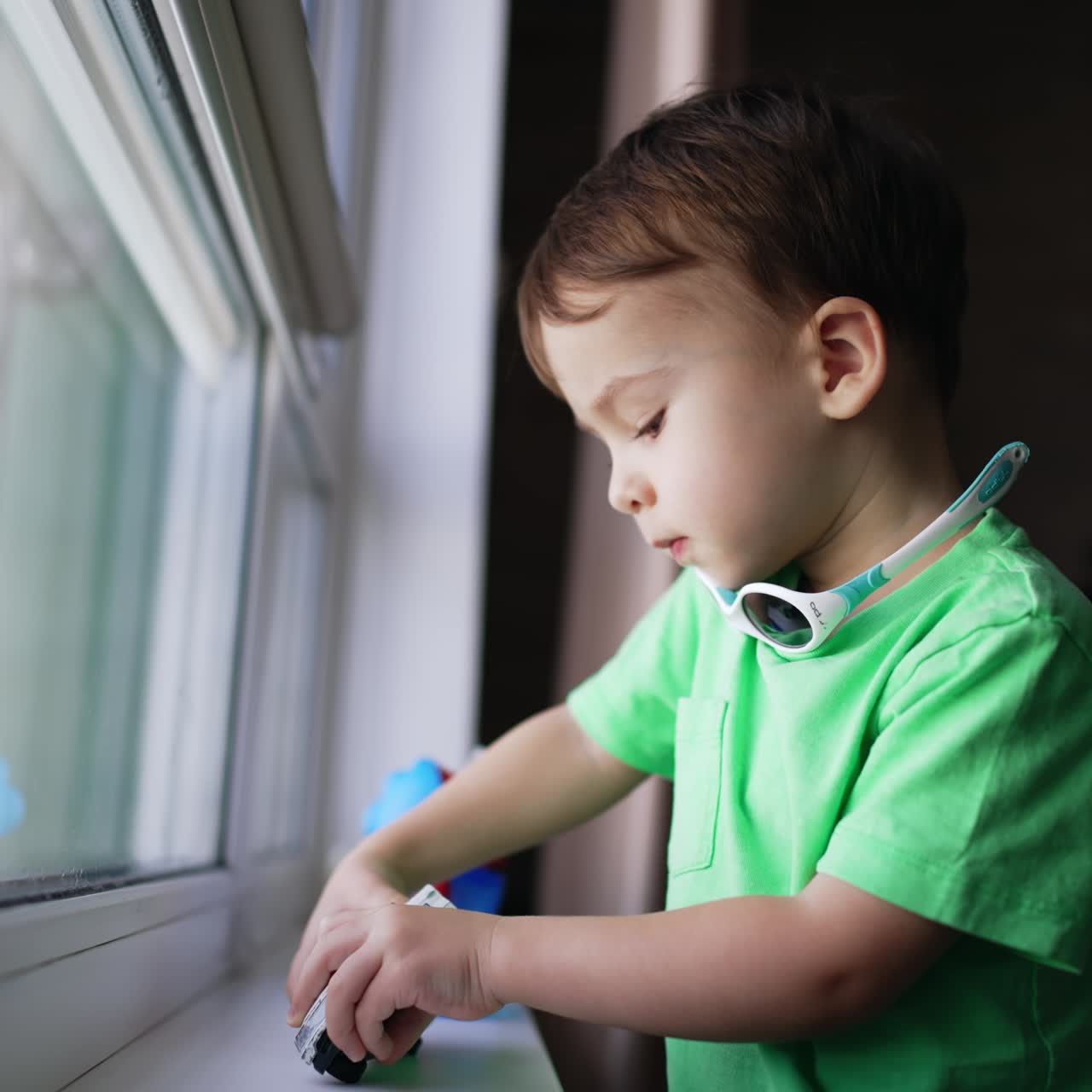 Un bebé adorable con las mejillas regordetas está de pie en la ventana sosteniendo un juguete. Un niño encantador jugando con un coche. Fondo borroso