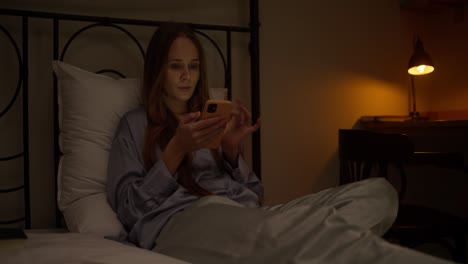 woman using phone in bed at night