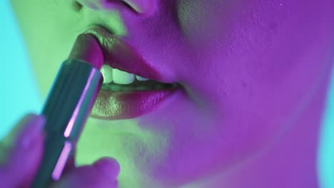 close up shot of woman lips while they are touched with a red lipstick to apply it with purple green light in her face of young woman while she is getting ready in slow motion