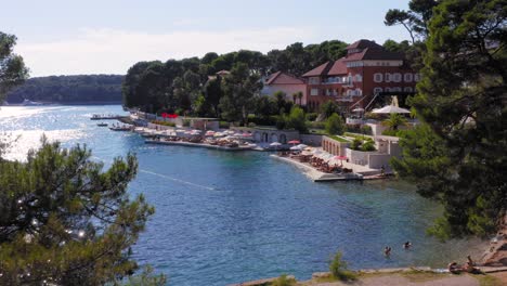 Small-sunny-bay-next-to-hotel-and-crowded-sea-deck-behind-tree-tops