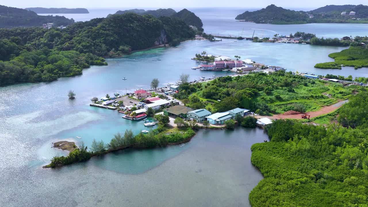 Ripresa aerea con drone rivela un villaggio su un'isola tropicale con acqua turchese e vegetazione lussureggiante.