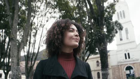 una mujer con un traje y cabello rizado camina por la ciudad de bogotá mientras escucha música, colombia