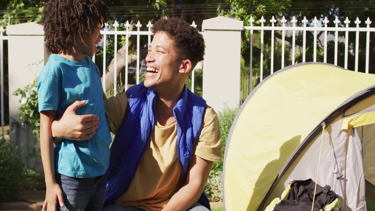 Happy biracial man and his son building tent together in garden