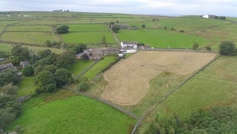 Drone-footage-panning-over-farmland-and-moorland-in-rural-Yorkshire,-including-country-roads-with-moving-vehicles,-a-country-pub,-stone-village-houses,-farm,-sheep-in-a-field-and-views-to-the-distance