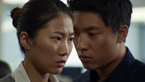 two individuals share a charged moment in a crowded office, navigating complex emotions and unexpressed desires. their close proximity hints at unresolved tension and potential conflict.