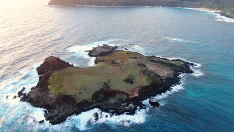 drone inclinándose hacia abajo sobre una mini isla privada en hawaii con oahu en el fondo