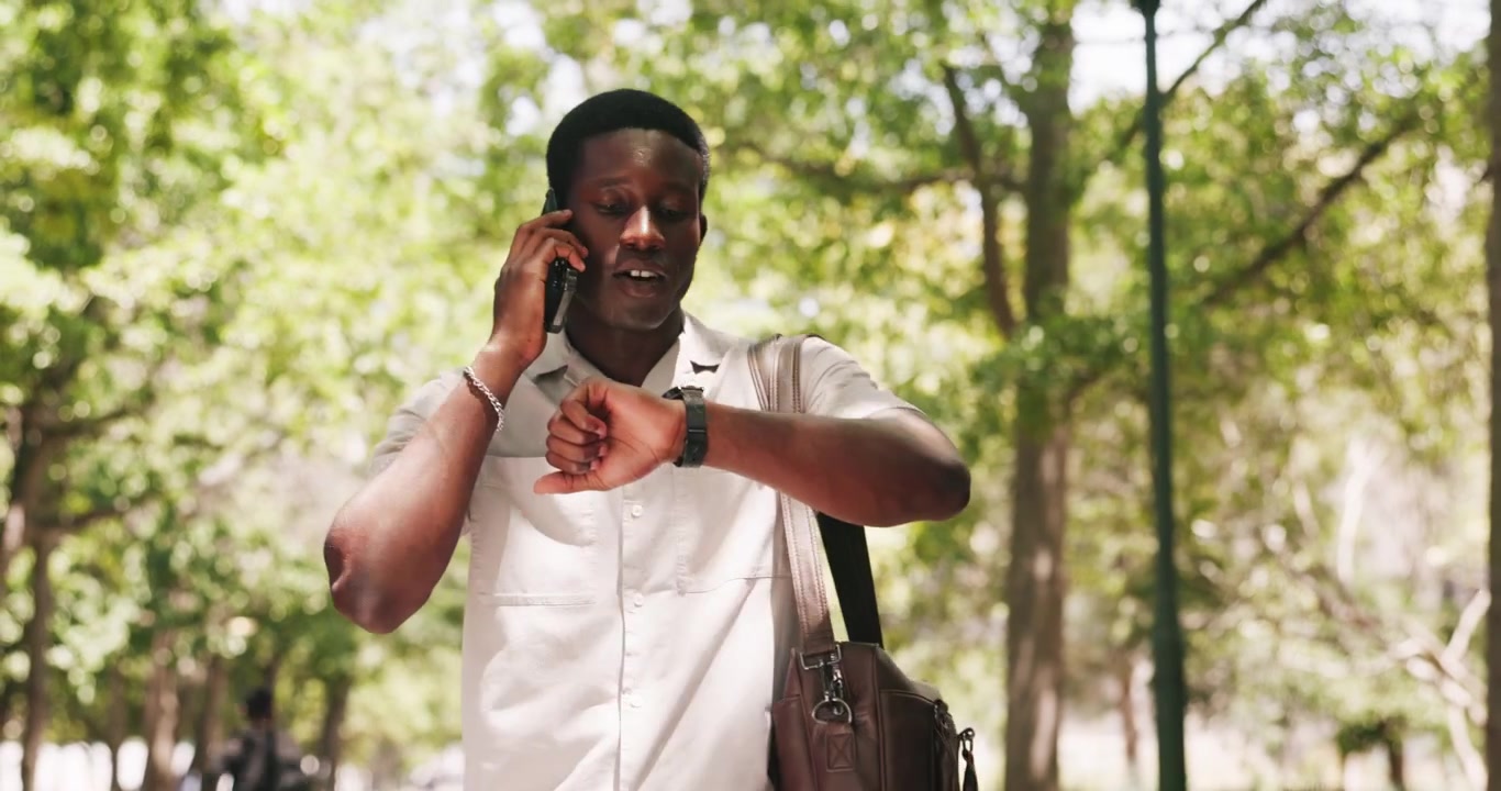 Young Man Walking in Park Talking on Smartphone and Checking Watch