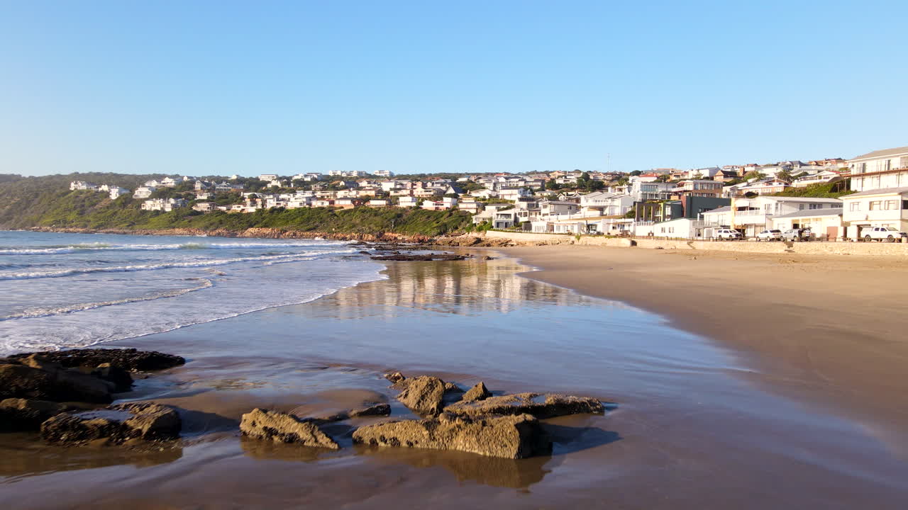 Low drone push-in over wet sand and small waves running onto Vleesbaai beach