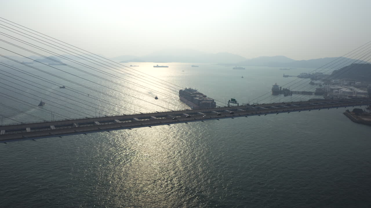 해가 질 때 대형 컨테이너선이 홍콩 항구에 진입하는 램블러 채널에서 멋진 전망을 감상할 수 있는 넓은 교수형 스톤커터 다리 위를 자동차가 지나갑니다.