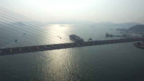 Los-Coches-Conducen-Por-El-Ancho-Puente-De-Los-Canteros-Colgantes-Con-Una-Gran-Vista-Sobre-El-Canal-Rambler-Donde-Un-Gran-Barco-De-Contenedores-Está-Entrando-En-El-Puerto-De-Hong-Kong-Durante-La-Puesta-De-Sol