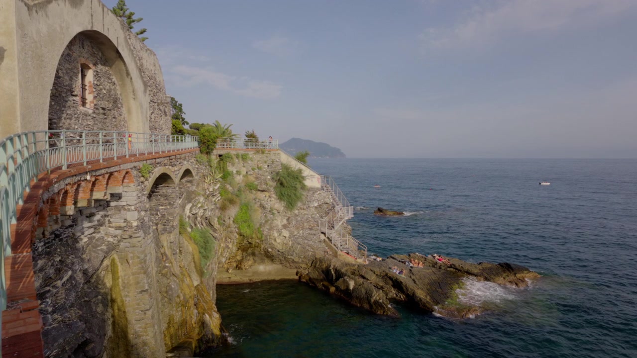 Des gens se détendent sur une côte rocheuse sous des arches de pierre historiques, au bord de la mer Ligure.
