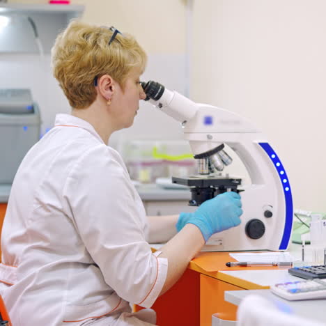 female scientist looks at biological samples under microscope. side view of a laboratory assistant working with modern microscope in medical clinic.