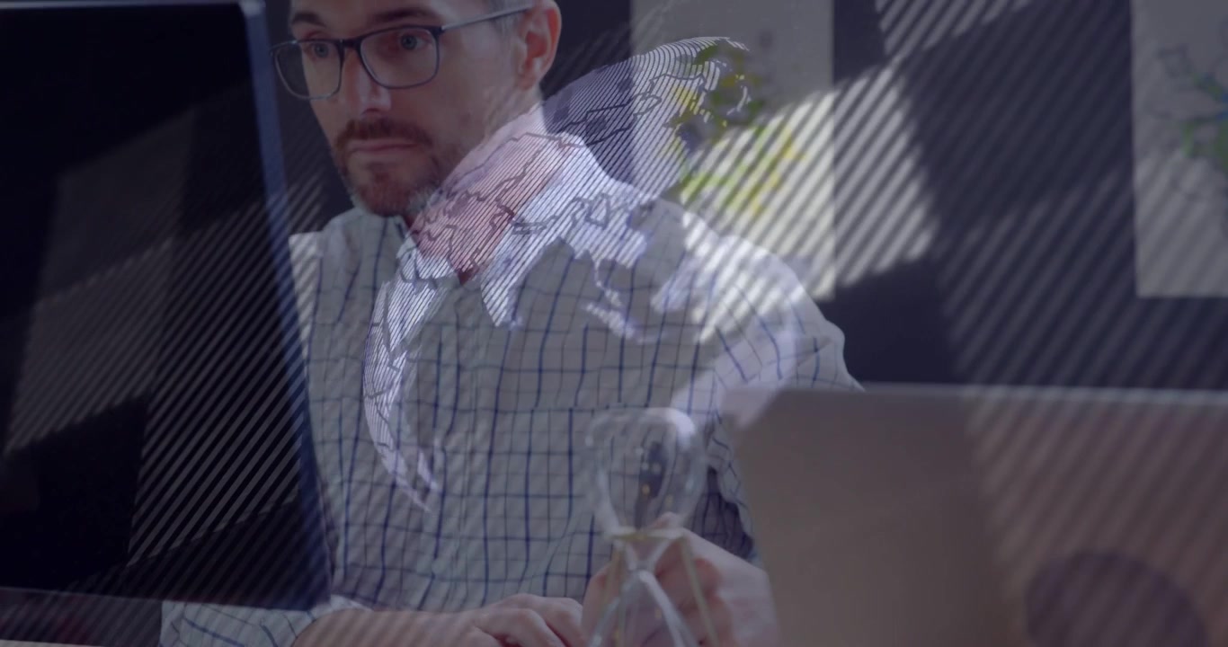 Man typing and flipping notes, causing overlays forming rotating map, touching hourglass for design
