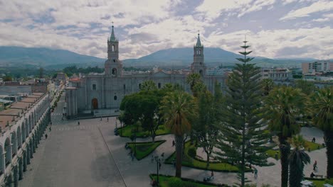 Drohnenaufnahmen-Aus-Der-Luft-über-Straßen-Und-Vegetation,-Die-Zur-Kathedrale-Von-Arequipa-Führen,-Abschließend-Mit-Einem-Blick-Auf-Den-Schneebedeckten-Vulkan-Misti-Nach-Einem-Regnerischen-Und-Bewölkten-Tag