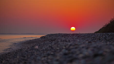 Timelapse-Del-Sol-En-Un-Cielo-Rojo-Escondido-Bajo-La-Arena-De-Una-Playa