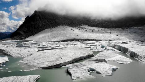 Spinning-aerial-flyover-above-icebergs-from-a-melting-glacier-lake-in-remote-parts-of-the-Swiss-Alps-on-a-sunny-day