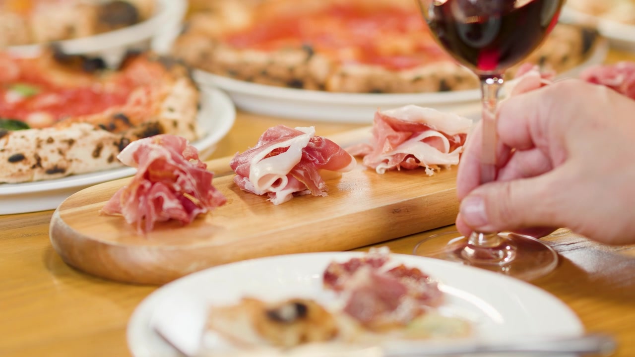 Persona che beve vino rosso a tavola con pizza e prosciutto