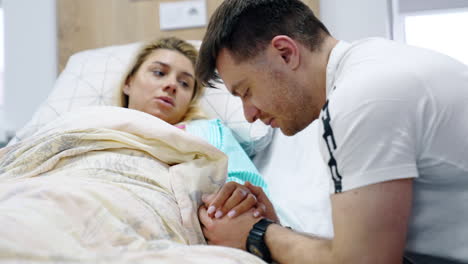 caucasia man kisses the hand of his wife lying in hospital ward. couple preparing for parenthood.