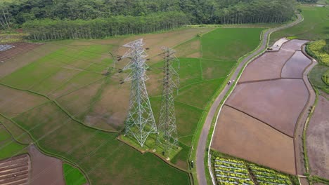 aerial drone shot over high voltage electricity tower in the middle of rice field - indonesia, asia