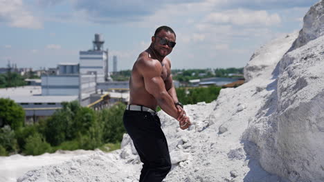 full length view of the attractive handsome muscle man with naked torso looking at his biceps and showing to the camera. american cheerful topless man