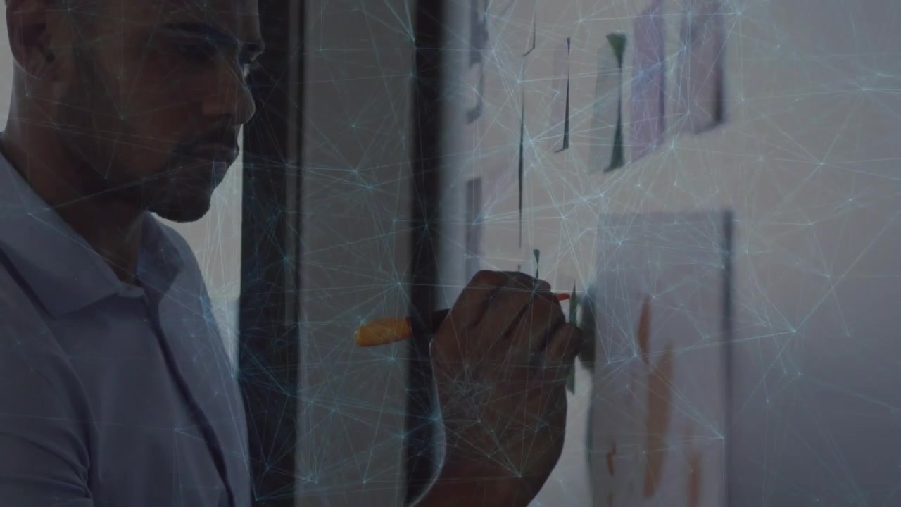 Man surveying sticky-note grid in workspace and writing business annotations to organize ideas