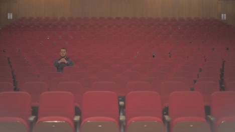 a tall white guy is in an empty theatre. he is the only one watching the show and he seems to be inspired with the performance while he pays closely attention to what he sees on stage