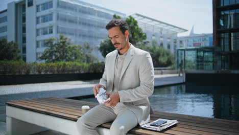 elegant boss unpacking lunch sunny park. business man enjoying sandwich at bench