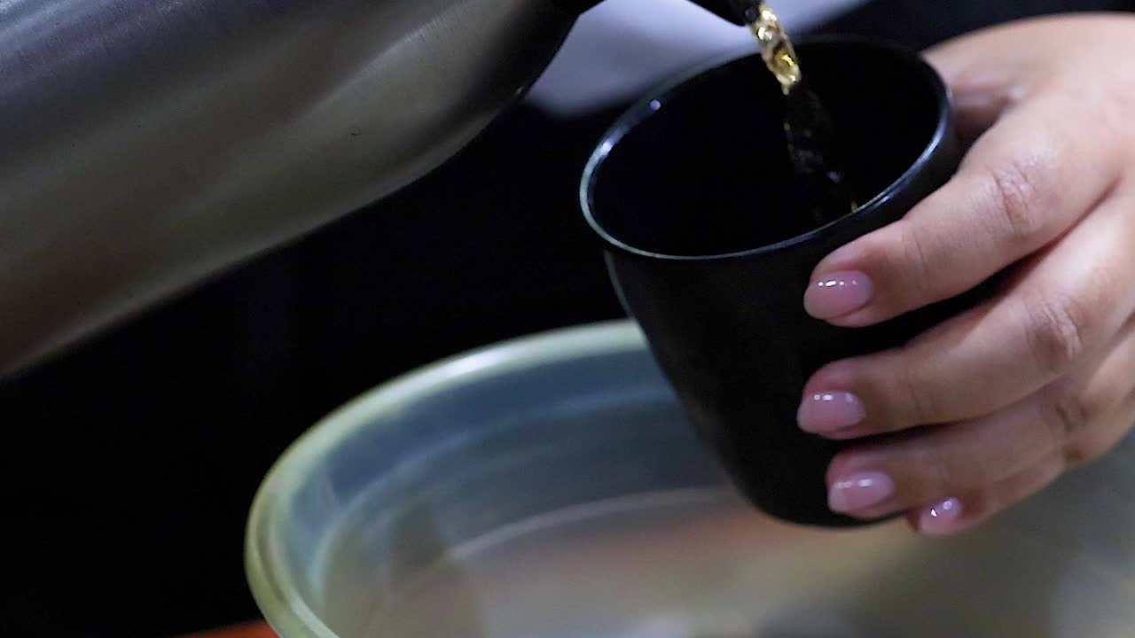 Extreme close-up of a person pouring tea from a thermos into a small black cup