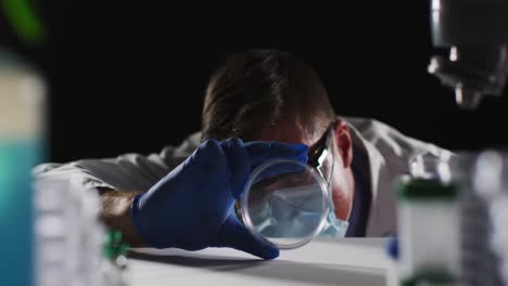 médico caucásico de sexo masculino con máscara facial y guantes inspeccionando la placa de petri