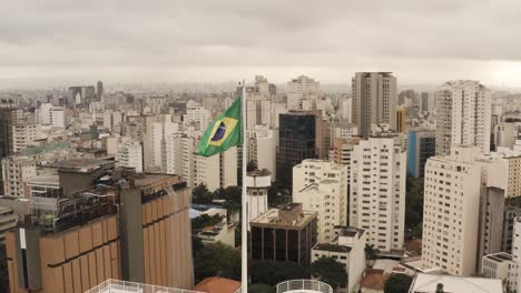 vista panorámica aérea que muestra la bandera brasileña en la parte superior del rascacielos y el paisaje urbano en el fondo