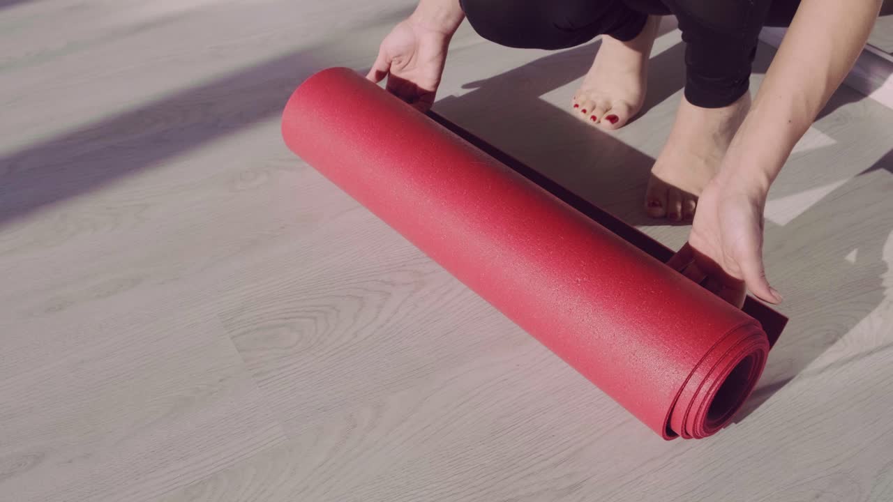 Unrolling a Vibrant Red Yoga Mat on a Wooden Floor, Preparing for a Relaxing Workout or Meditation Session with Natural Light Filtering In