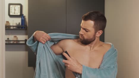 portrait of young man using antiperspirant body spray in bathrobe