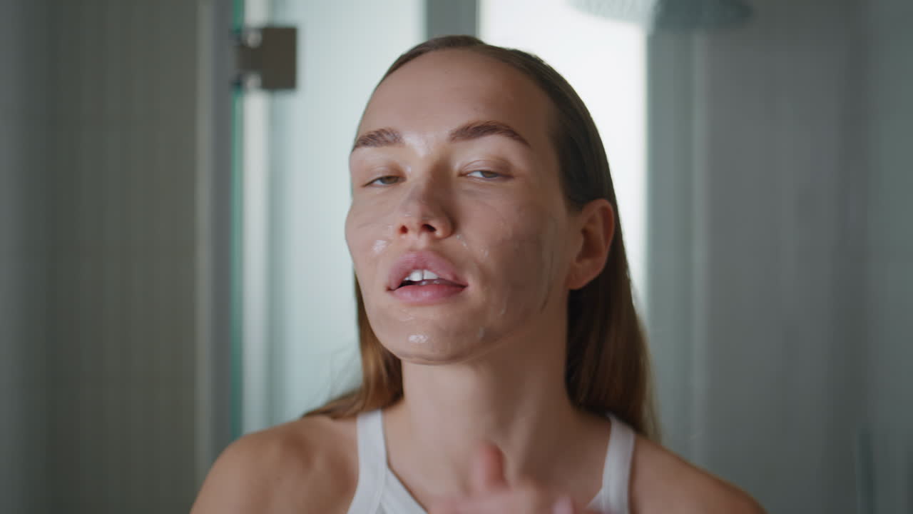 Woman applying facial mask in bathroom closeup. Pretty girl enjoy skin therapy
