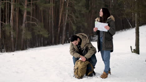 caucasian couple checking map for directions in a snowed forest.